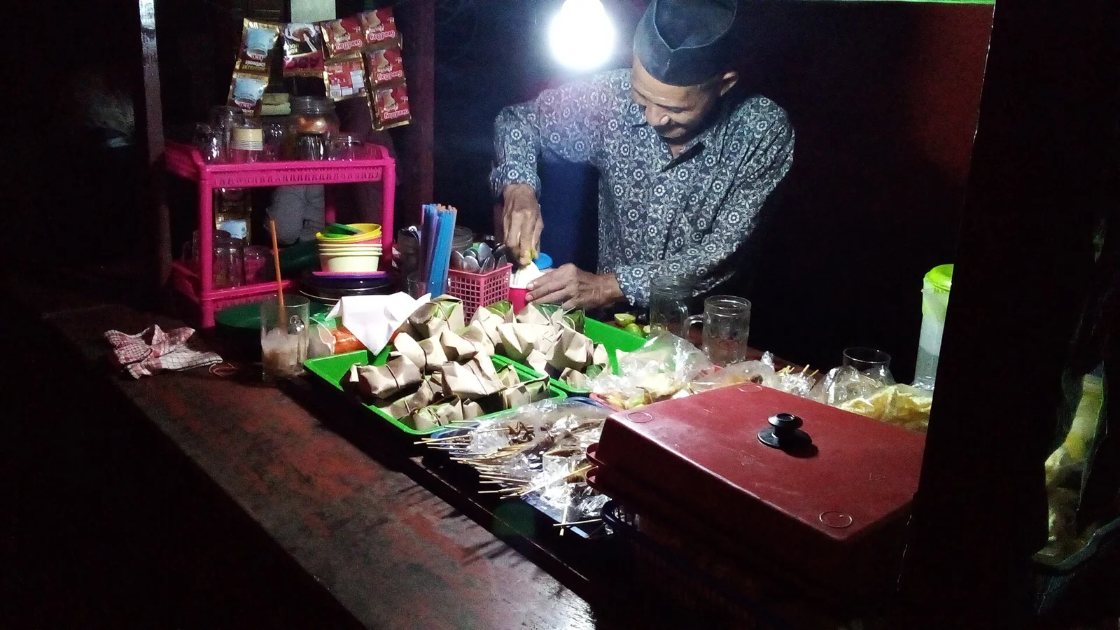 Penjual angkringan menyiapkan sate dan gorengan di warung malam hari