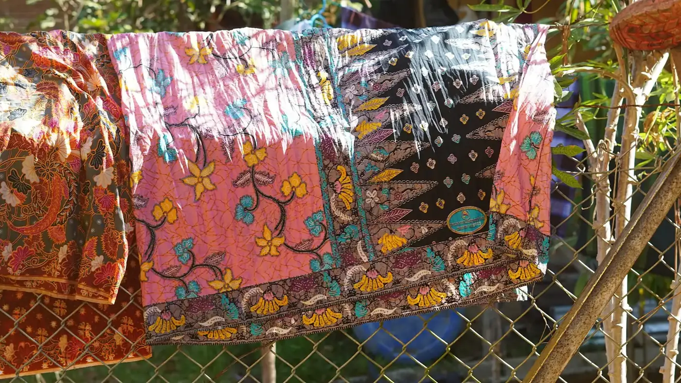 Beberapa lembar kain batik warna-warni digantung di pagar kawat