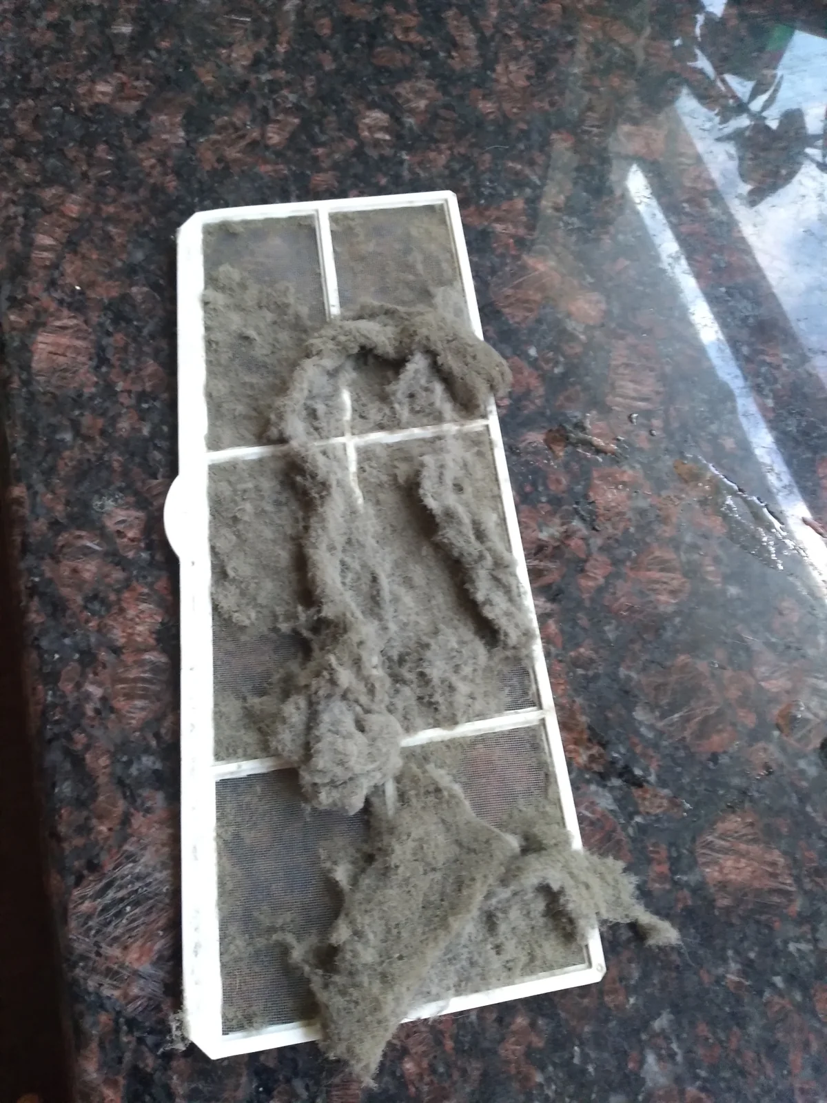 Filter AC split berwarna putih tertutup gumpalan debu abu-abu di atas meja granit