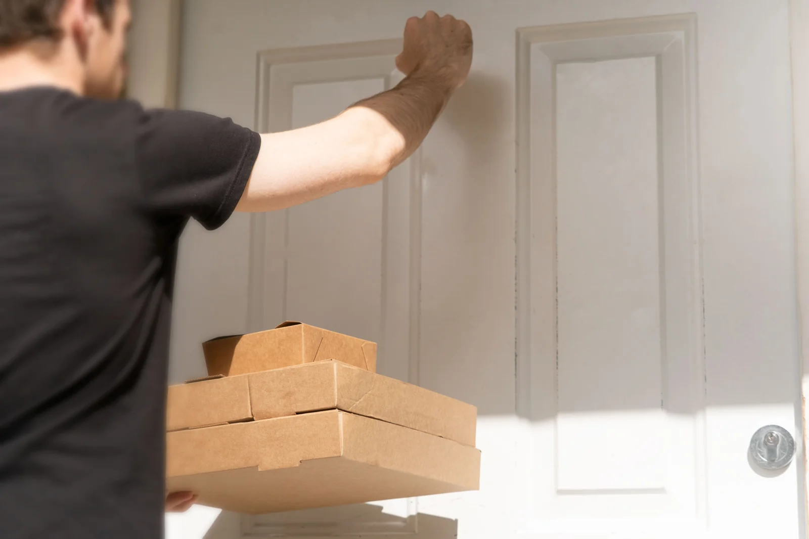 Kurir mengetuk pintu rumah dengan tumpukan paket kardus di depannya