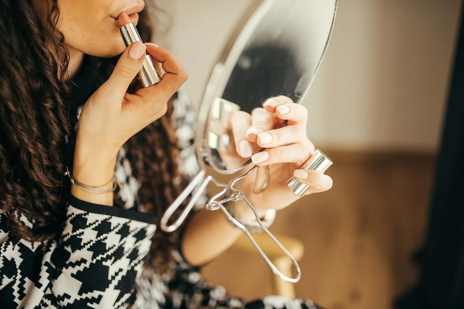 Perempuan mengoleskan lipstik sambil memegang cermin kecil
