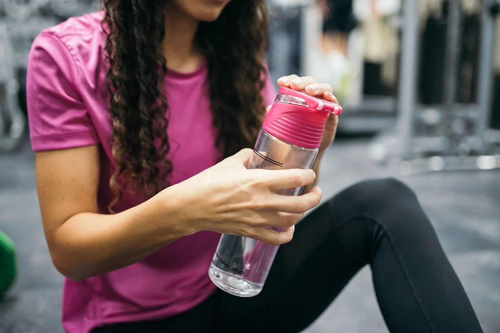 Perempuan berambut keriting duduk di lantai dan bersiap minum dari botol