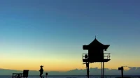 Siluet perempuan berlari melewati menara penjaga pantai saat matahari terbit