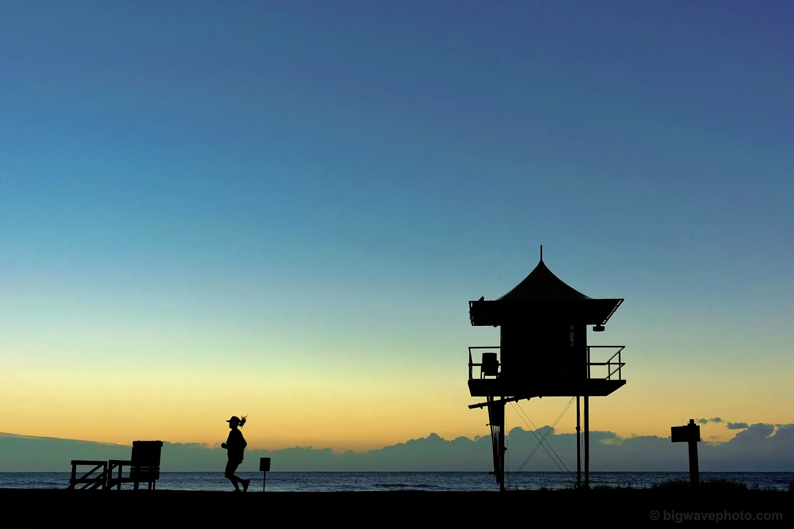 Siluet perempuan berlari melewati menara penjaga pantai saat matahari terbit