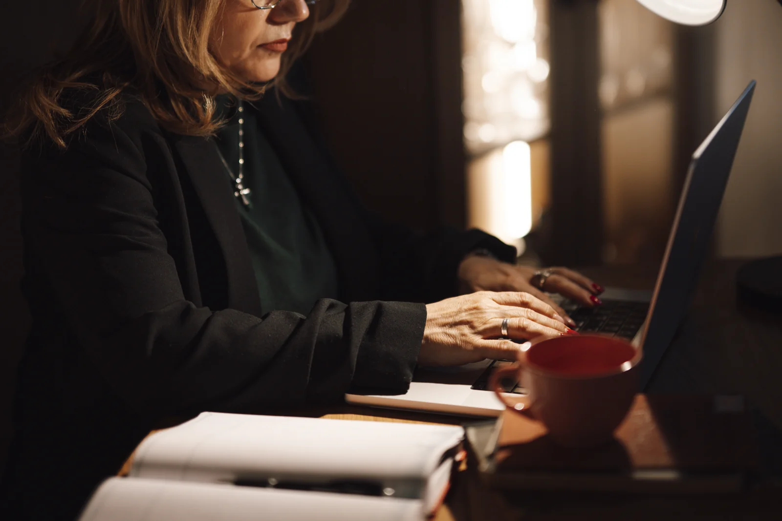 Perempuan mengetik di laptop dengan buku catatan dan secangkir kopi di meja kerja