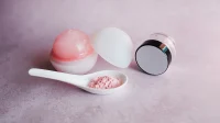 produk-skincare-latar-merah-muda Beberapa jar produk skincare dan sendok berisi bubuk merah muda di atas latar merah muda