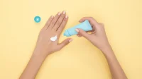 Skincare musim pancaroba - pelembap Tangan perempuan mengoles krim pelembap dari tube biru di atas latar kuning