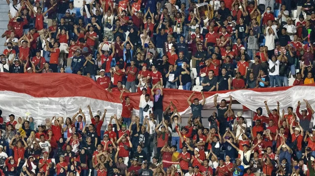 Tribun penuh suporter Indonesia berbaju merah membentangkan bendera Merah Putih raksasa