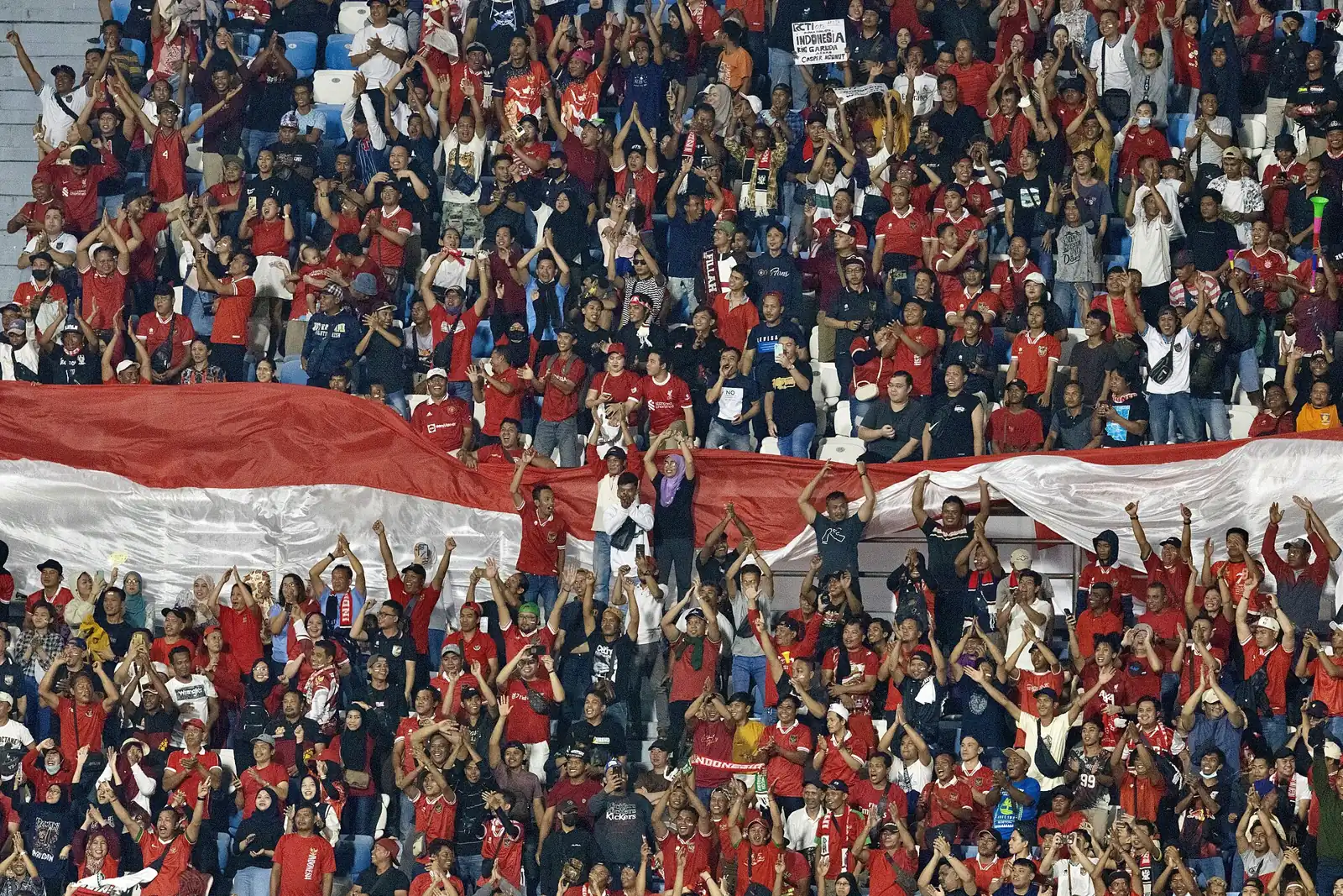 Tribun penuh suporter Indonesia berbaju merah membentangkan bendera Merah Putih raksasa