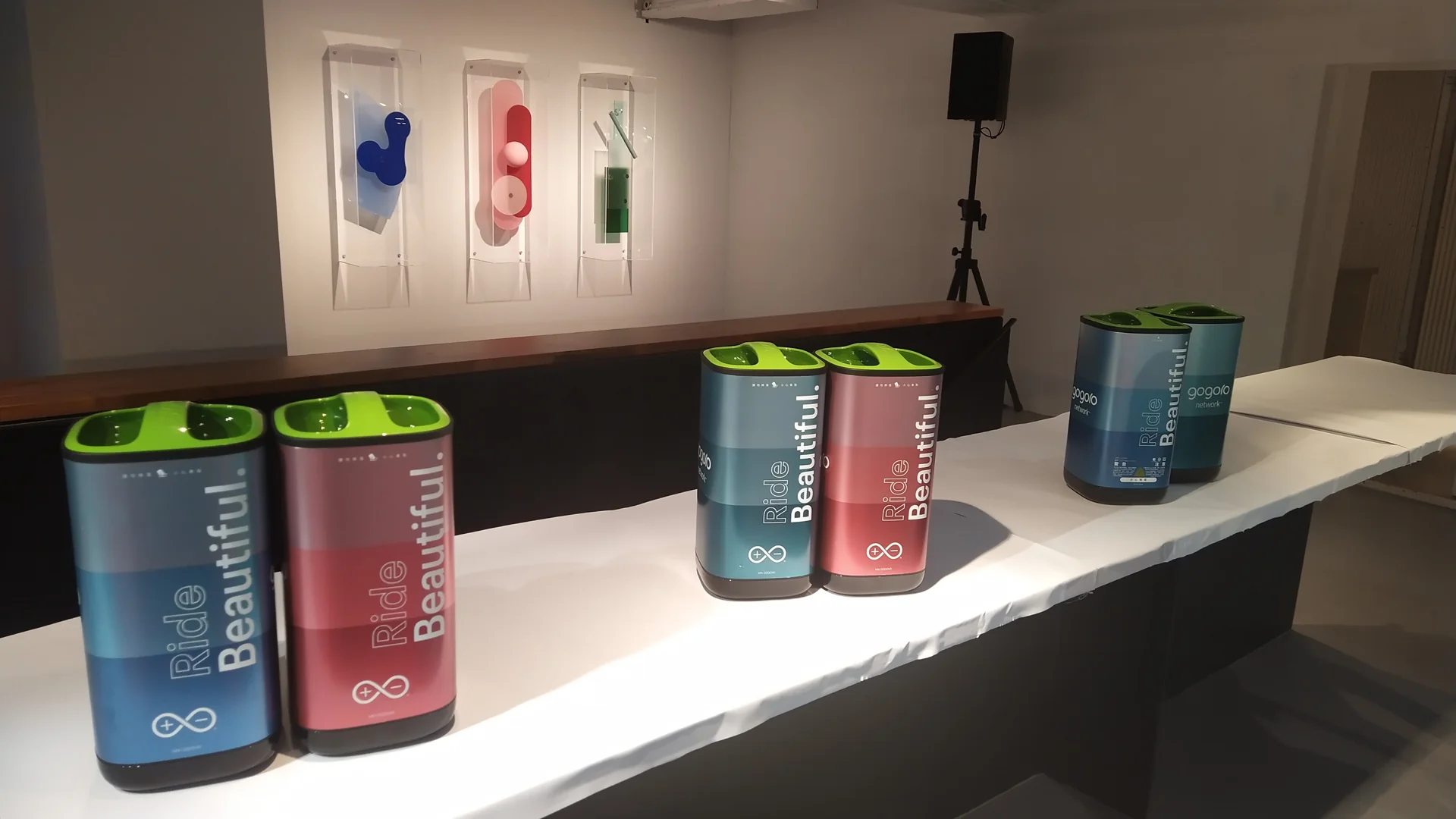 Deretan baterai skuter listrik Gogoro berwarna biru, merah, dan hijau di atas meja pameran