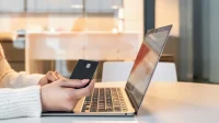 Tangan memegang kartu pembayaran di depan laptop, ilustrasi belanja online aman 11.11