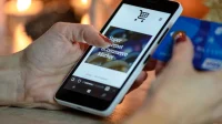 Tangan memegang ponsel dengan ikon keranjang belanja di layar dan kartu pembayaran
