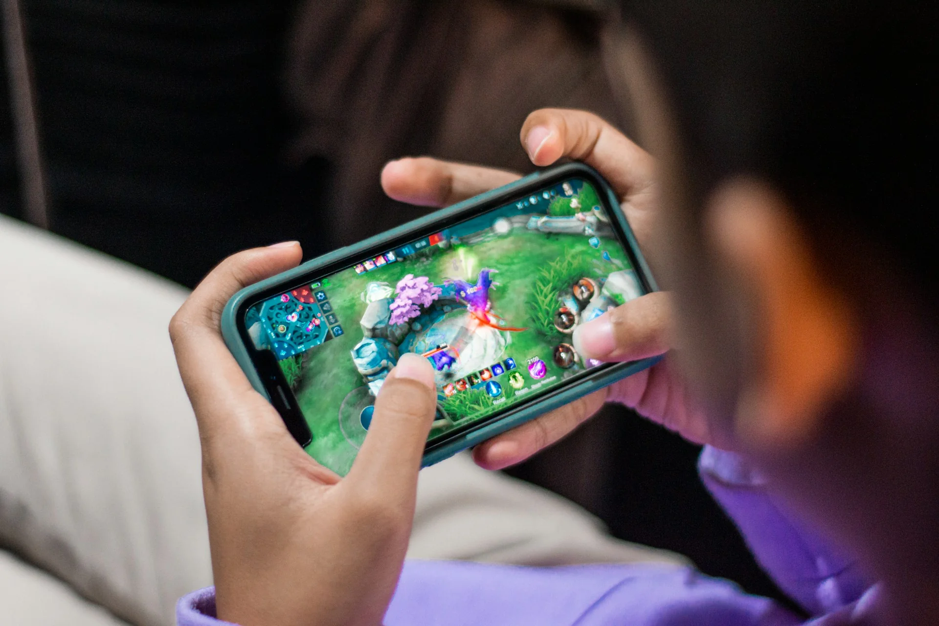 Kedua tangan memegang smartphone dalam posisi landscape saat bermain game MOBA