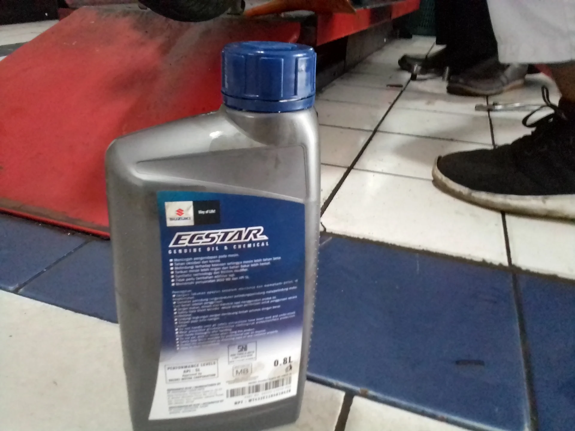 Botol oli mesin sepeda motor 4 tak isi 0,8 liter berlabel spesifikasi API dan JASO MB di lantai bengkel
