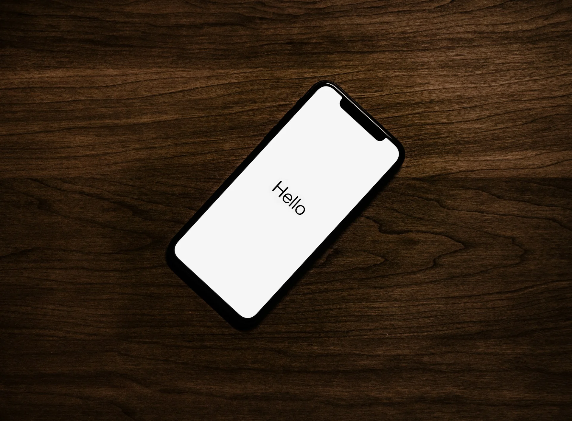 iPhone di atas meja kayu gelap menampilkan layar penyiapan bertuliskan Hello