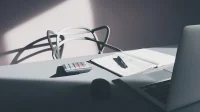 kalkulator-buku-catatan-laptop-meja-kerja Kalkulator, buku catatan berisi hitungan tulisan tangan, pulpen, dan laptop di atas meja kerja