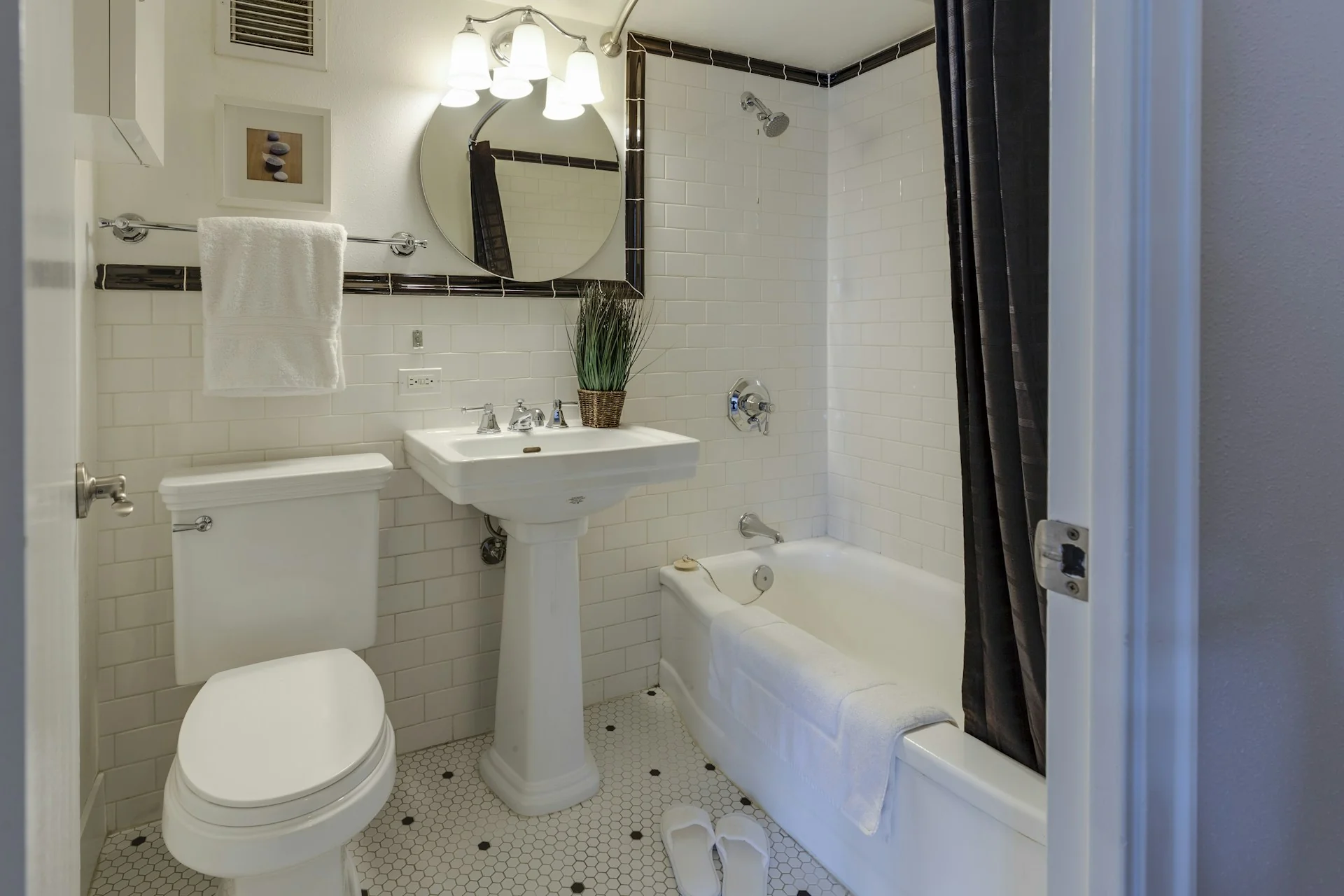 Kamar mandi bersih dengan keramik putih, wastafel, kloset, dan bak mandi bertirai gelap