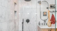 Kamar mandi dengan shower Kamar mandi berdinding marmer putih dengan rain shower hitam, keran pengatur, dan wastafel kayu