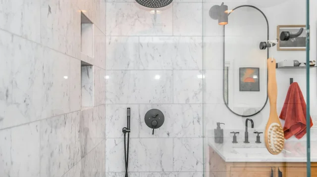 Kamar mandi berdinding marmer putih dengan rain shower hitam, keran pengatur, dan wastafel kayu