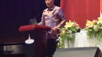 Luhut Binsar Pandjaitan berpidato di balik podium merah dengan mikrofon dan rangkaian bunga