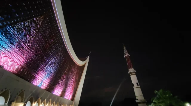 Atap gonjong Masjid Raya Sumatera Barat di Padang dengan lampu warna-warni dan menara pada malam hari