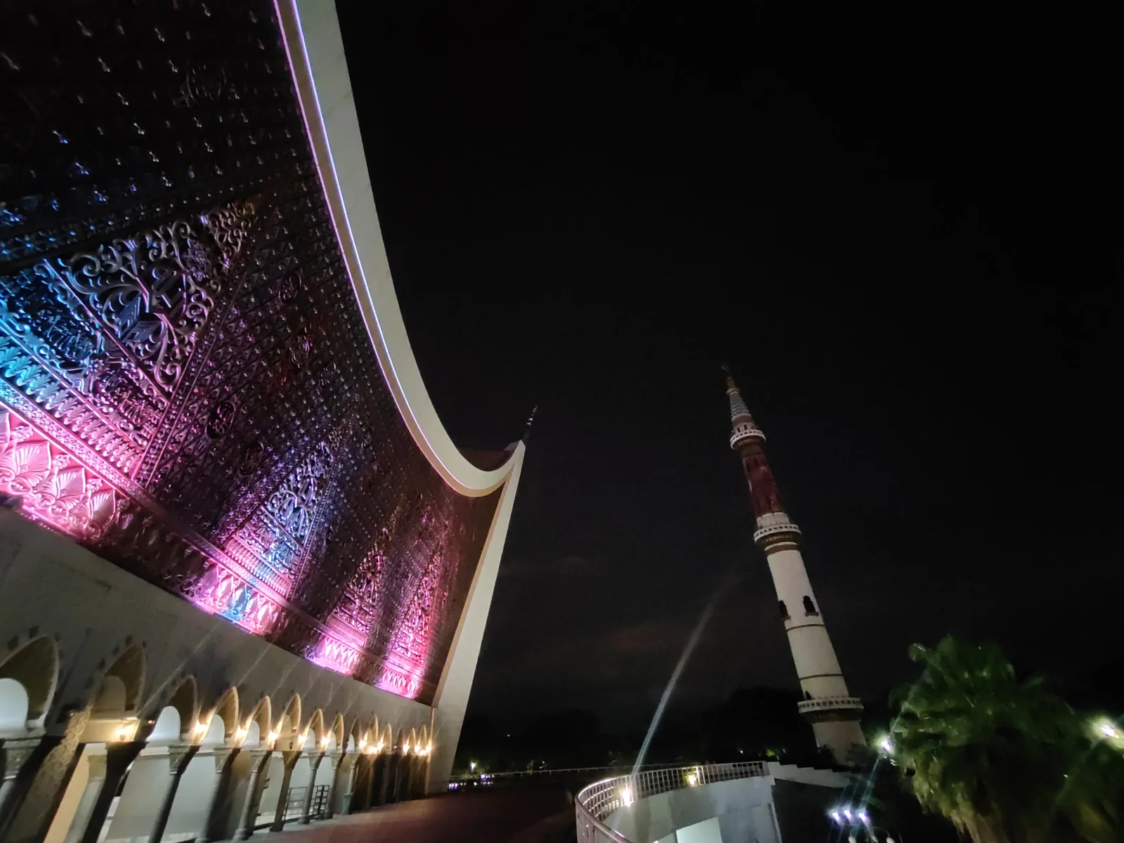 Atap gonjong Masjid Raya Sumatera Barat di Padang dengan lampu warna-warni dan menara pada malam hari