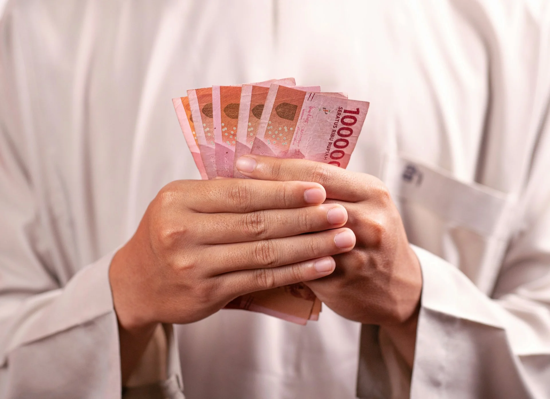 Tangan memegang lembaran uang Rp100.000, gambaran hasil jual emas batangan