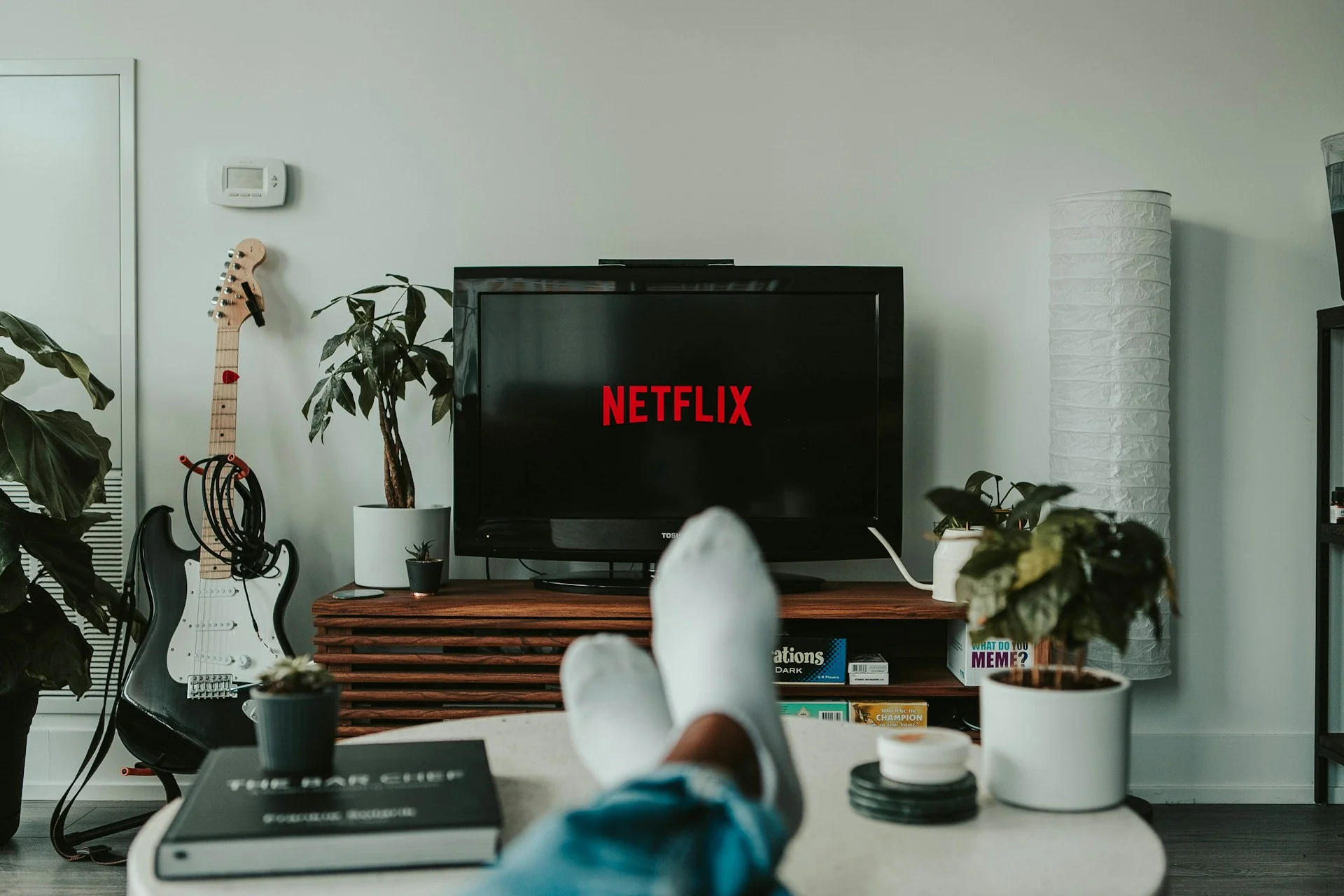 Kaki berkaus kaki putih di atas meja menghadap TV yang membuka aplikasi streaming di ruang keluarga