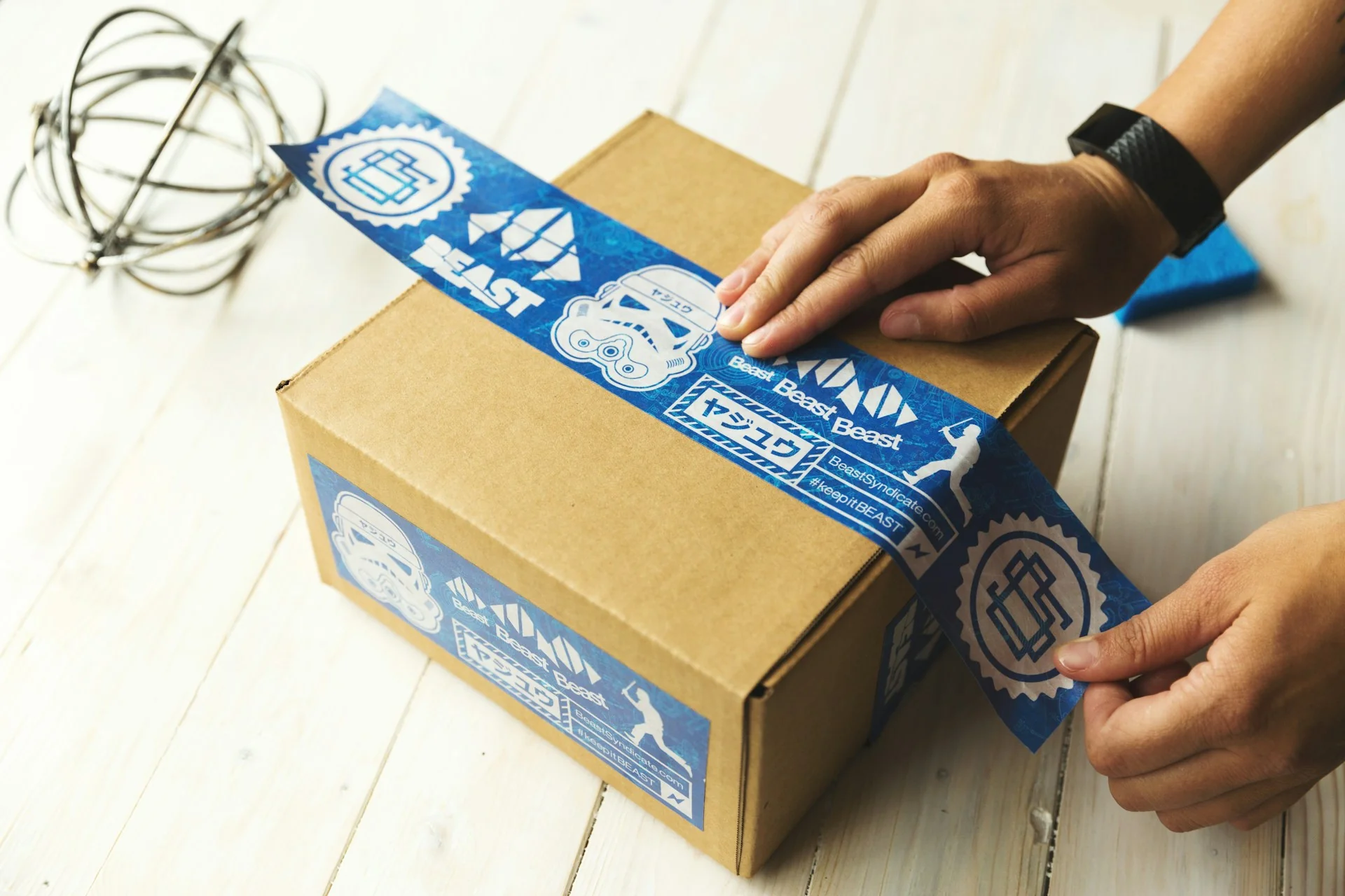 Tangan menyegel kardus paket stok barang jualan online dengan lakban biru di atas meja kayu putih
