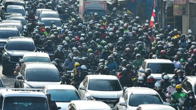 Ratusan pengendara sepeda motor memadati jalan kota di Indonesia, gambaran pilihan motor listrik vs motor bensin