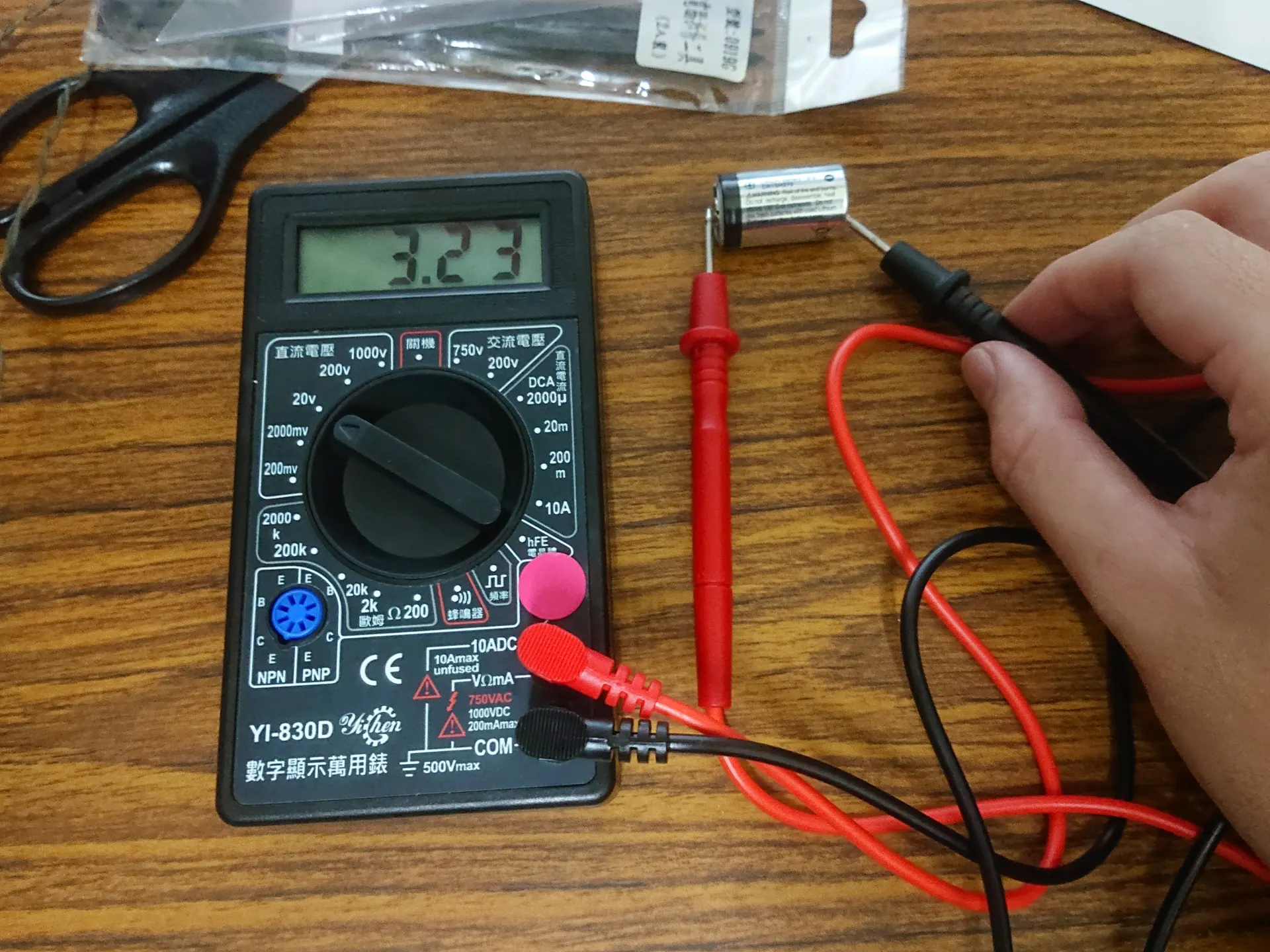 Multimeter digital mengukur tegangan baterai dengan probe merah dan hitam