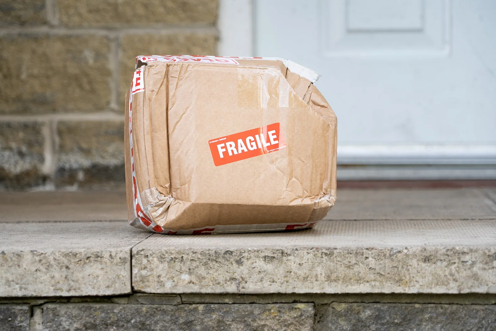 Paket kardus penyok berstiker fragile tergeletak di depan pintu rumah