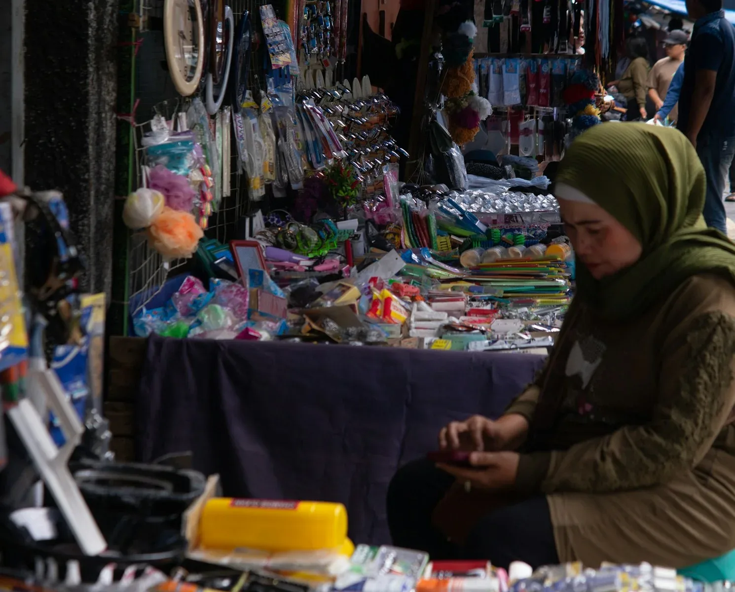 Pedagang perempuan di lapak pasar Garut memeriksa ponsel, ilustrasi cara hitung dan bayar PPh final UMKM