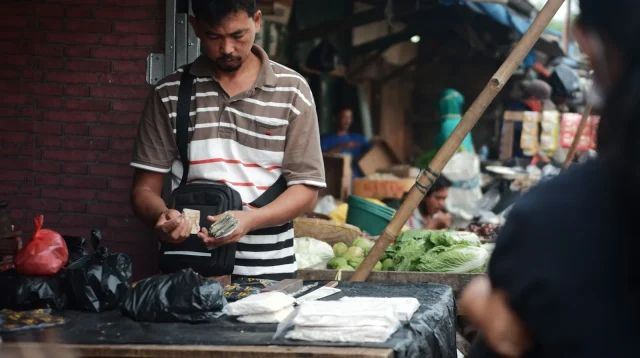 Pedagang di pasar tradisional menghitung uang hasil jualan, gambaran pencatatan omzet harian UMKM
