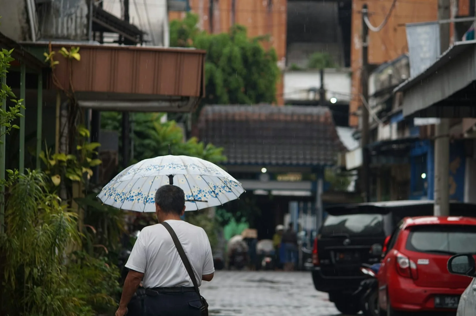 Pria berpayung berjalan di gang basah saat musim hujan 2026