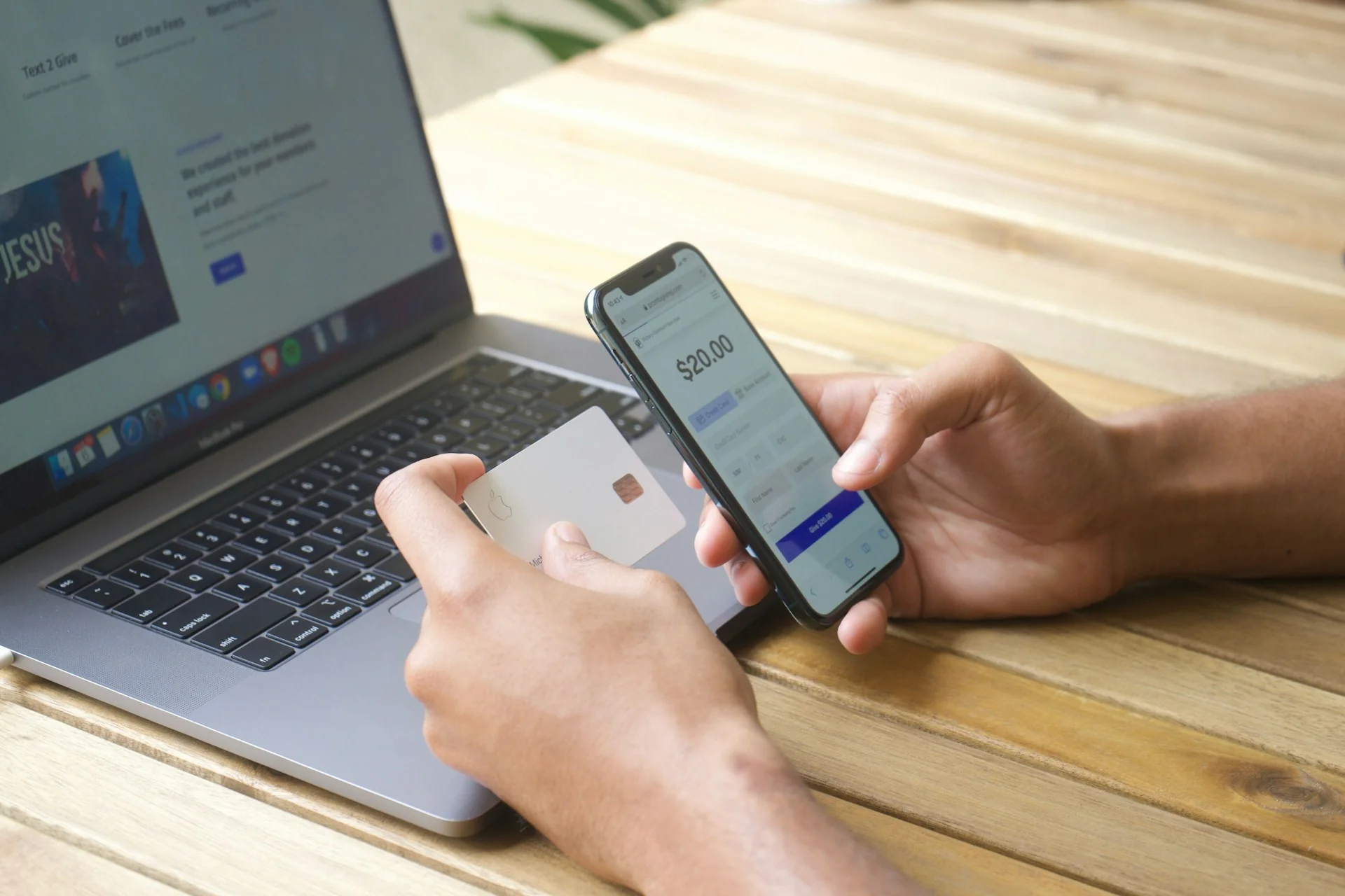 Tangan memegang kartu pembayaran dan ponsel berisi layar pembayaran di depan laptop