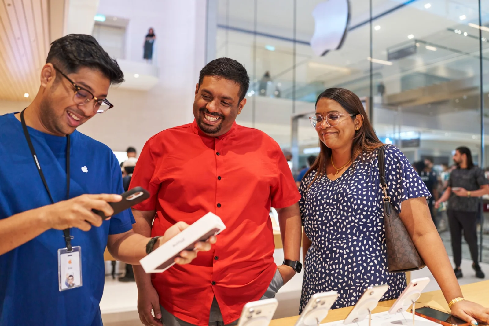 Staf Apple berbaju biru memegang kotak iPhone 18 Pro dan melayani dua pembeli di Apple Store