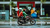 Pengendara motor saat hujan Dua pengendara motor berjaket dan jas hujan melintas di jalan basah saat hujan