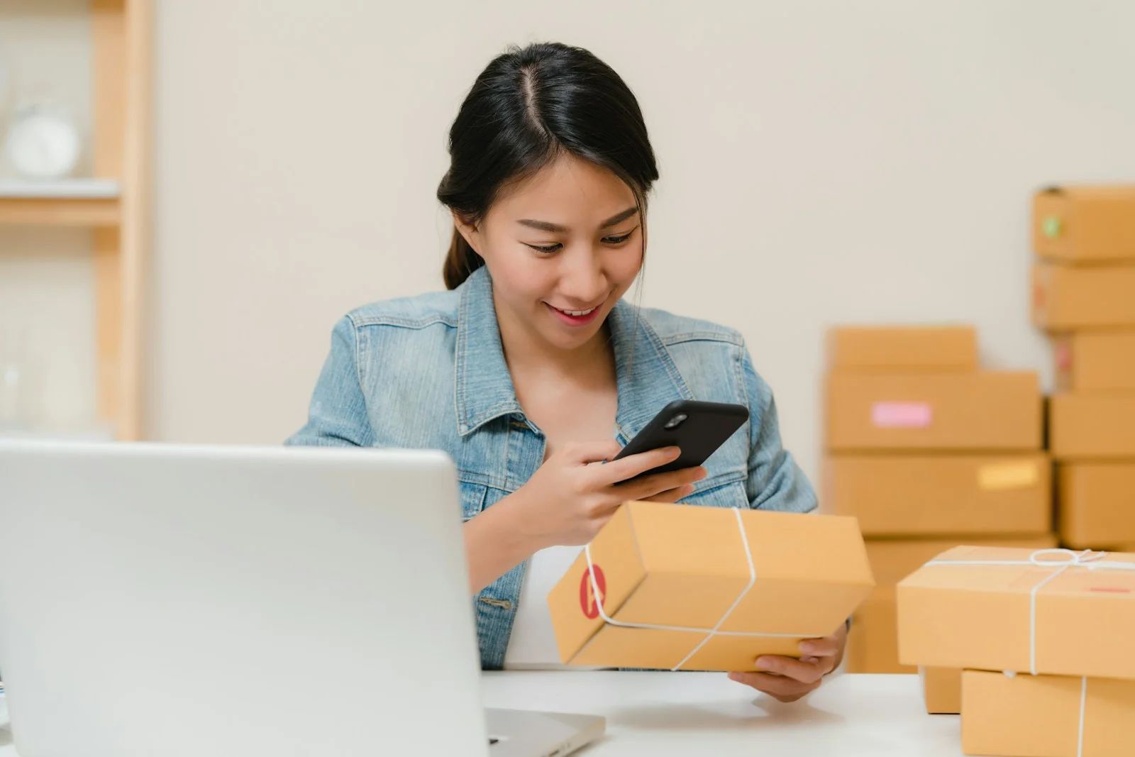 Penjual mengemas paket pesanan jualan online untuk pemula sambil memotret label dengan ponsel