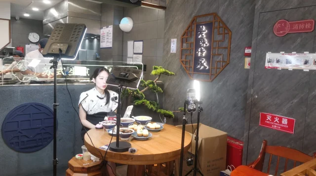 Cara jualan live: penjual siaran langsung memperkenalkan produk makanan di depan HP bertripod dan lampu LED