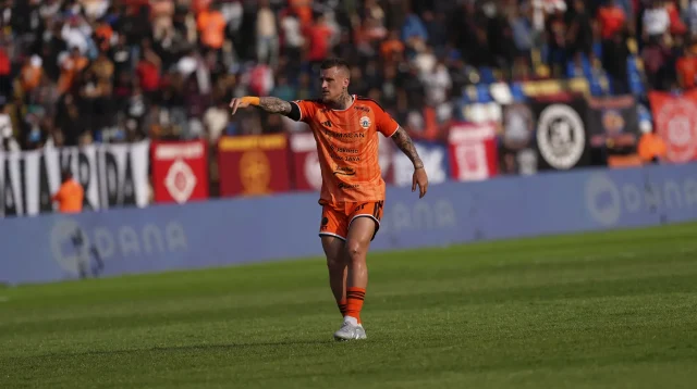 Pemain Persija Jakarta berseragam oranye memberi arahan di lapangan dengan latar suporter