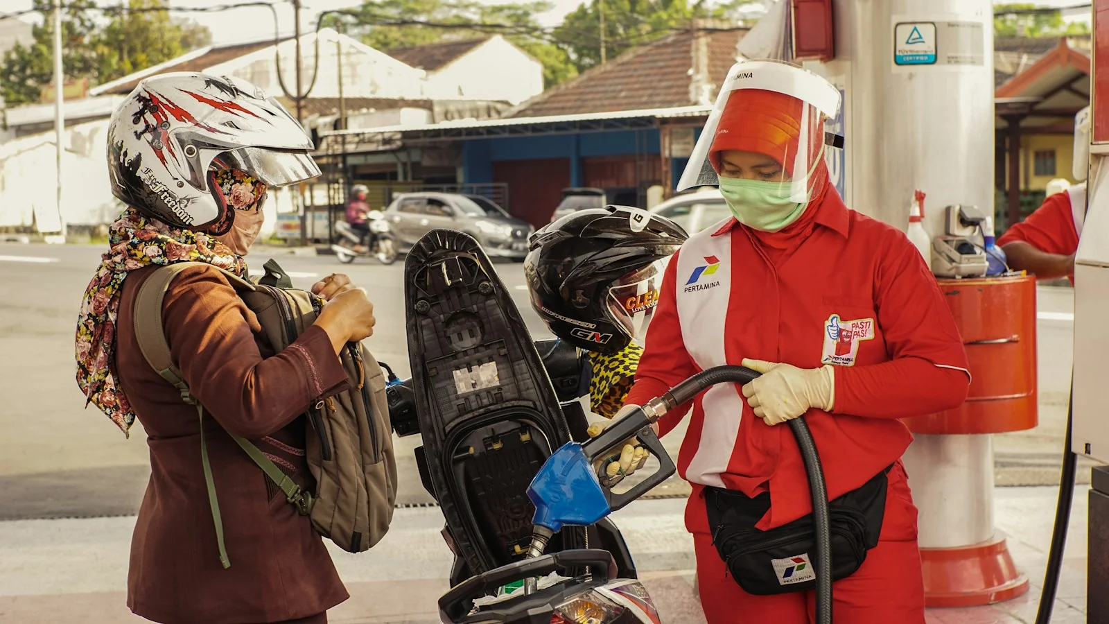 Petugas SPBU Pertamina berseragam merah mengisi bensin ke tangki skuter milik pengendara berhelm