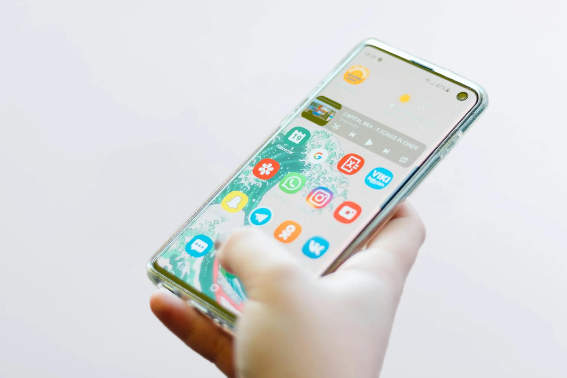 Tangan memegang ponsel Android di layar utama dengan ikon WhatsApp terlihat