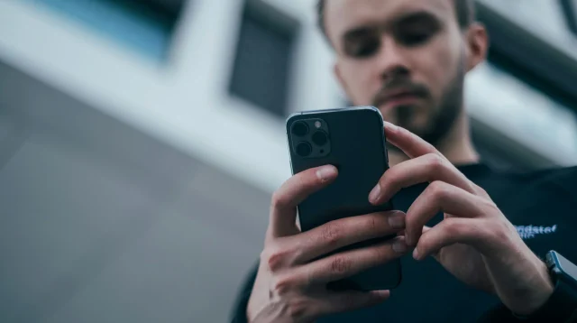Pria berkaus hitam memegang smartphone dengan dua tangan dan menatap layarnya