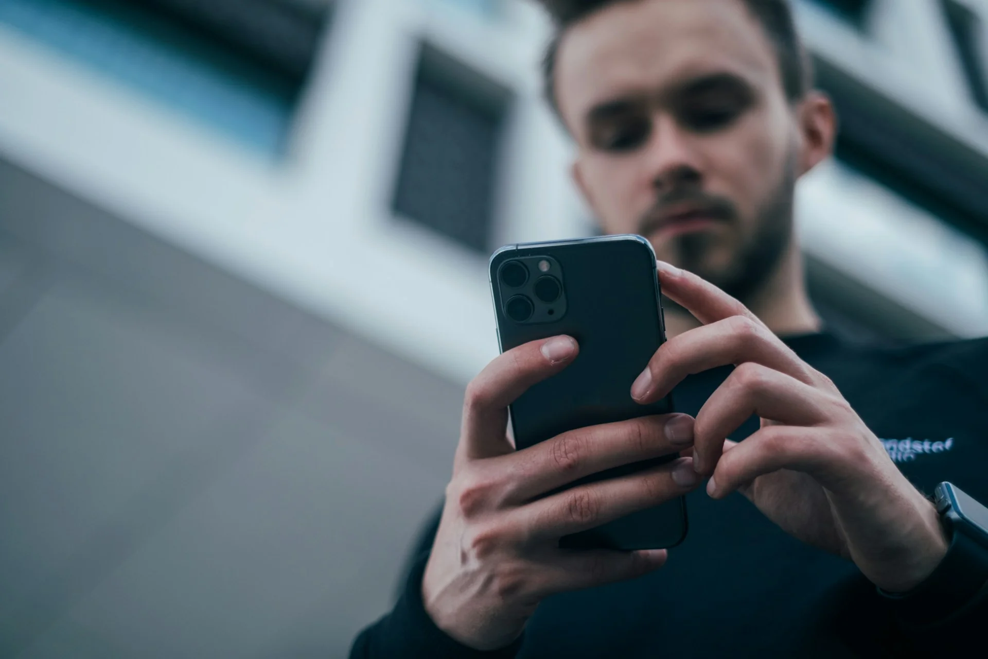 Pria berkaus hitam memegang smartphone dengan dua tangan dan menatap layarnya