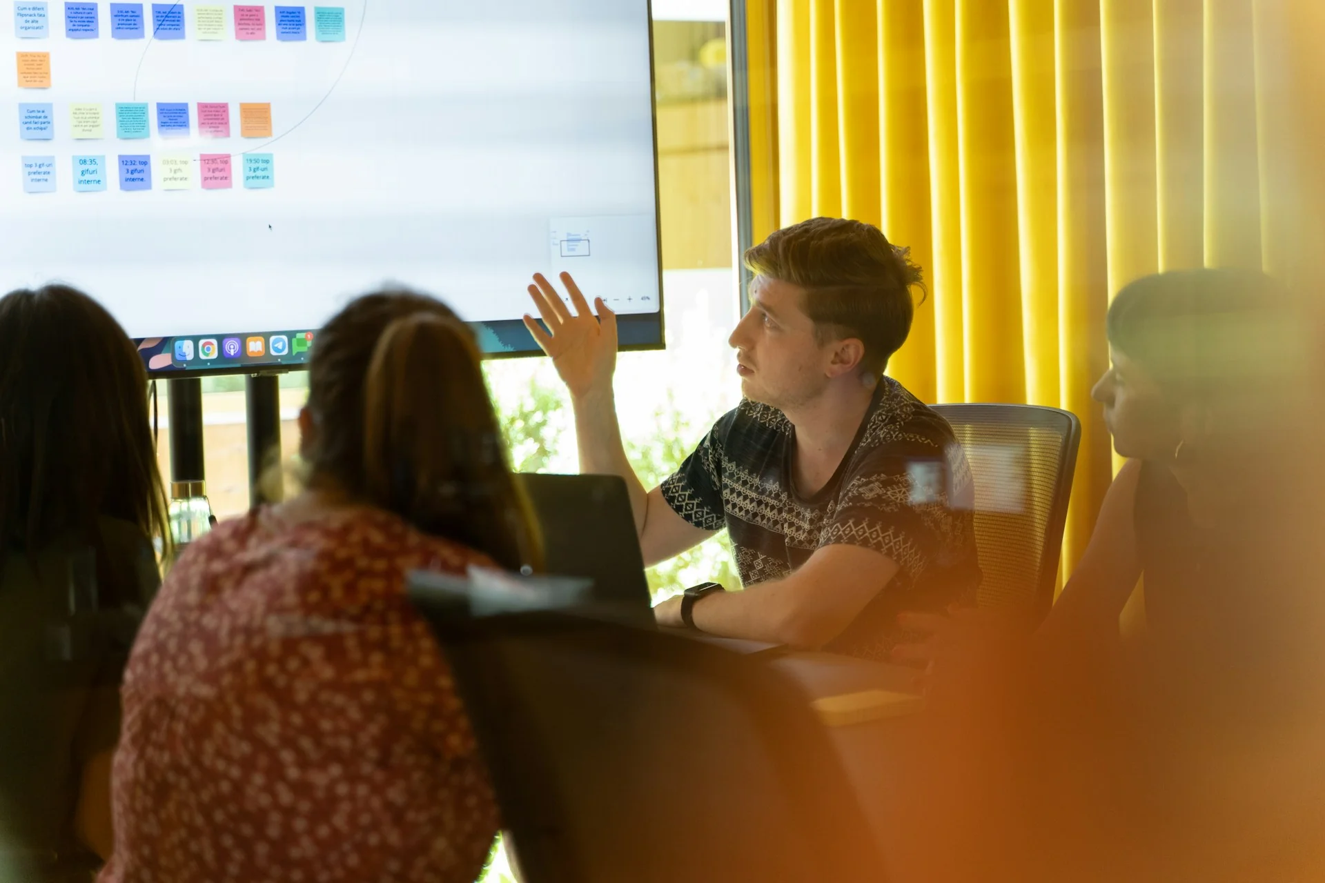 Pria menunjuk layar besar berisi catatan tempel digital saat rapat bersama rekan kerja di ruang meeting