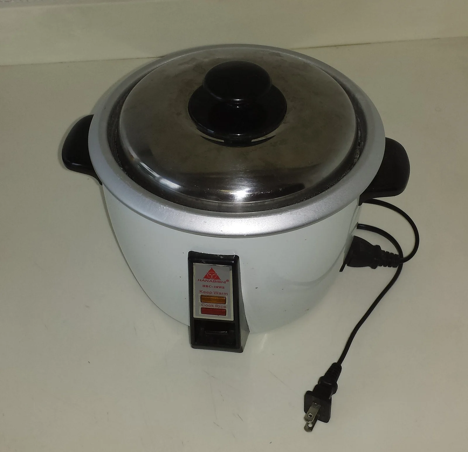Rice cooker putih berkabel dengan tutup kaca di atas meja