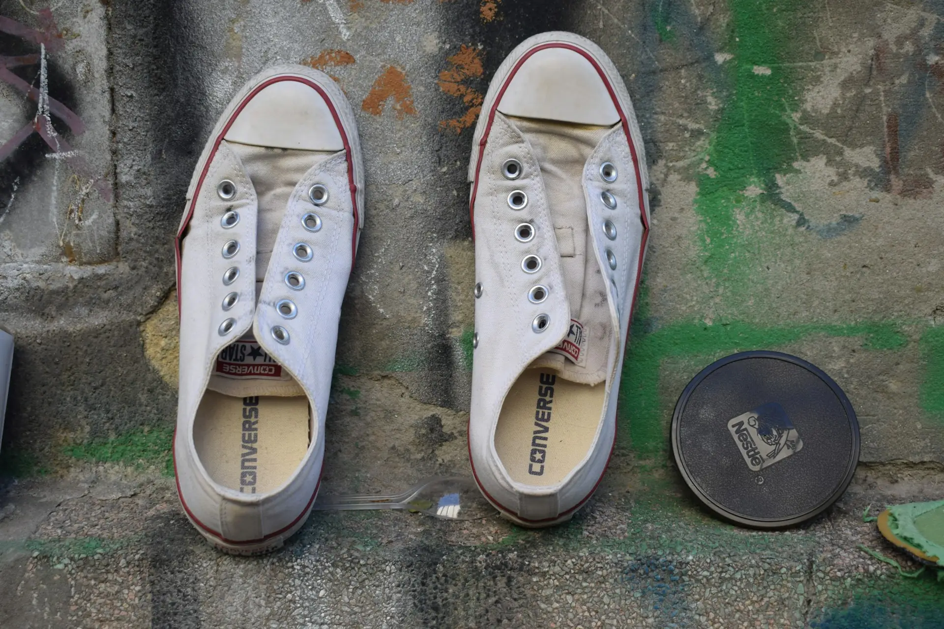 Sepasang sepatu kanvas putih Converse tanpa tali di atas lantai beton bercoretan