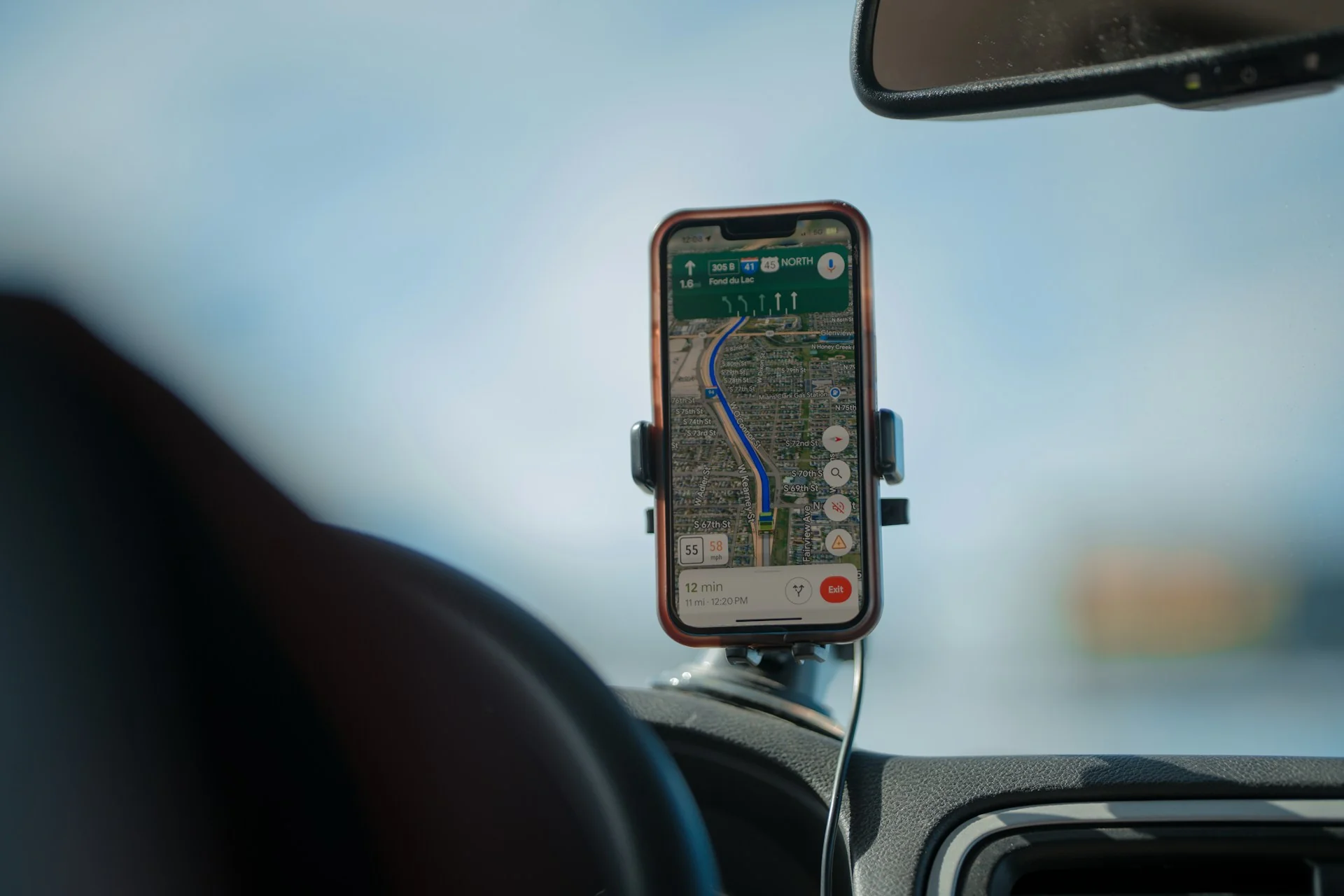 Smartphone di holder kaca depan mobil menampilkan rute navigasi peta dengan kabel daya tersambung