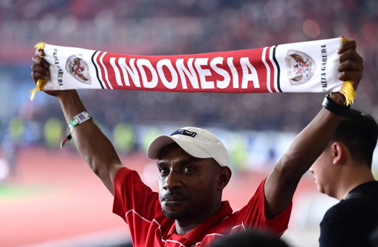 Suporter Timnas Indonesia berkaus merah membentangkan syal bertuliskan Indonesia di tribun SUGBK